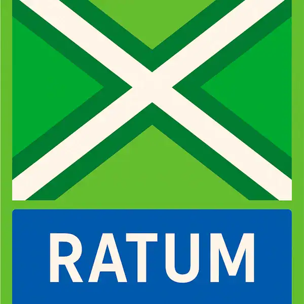Plaatsnaambord met de tekst "RATUM" in witte hoofdletters op een blauwe balk. Daarboven een vlag met lichtgroene achtergrond, een helder wit St. Andrieskruis gecentreerd in een donkergroen kruispatroon — conform het originele vlagontwerp van de Achterhoek.