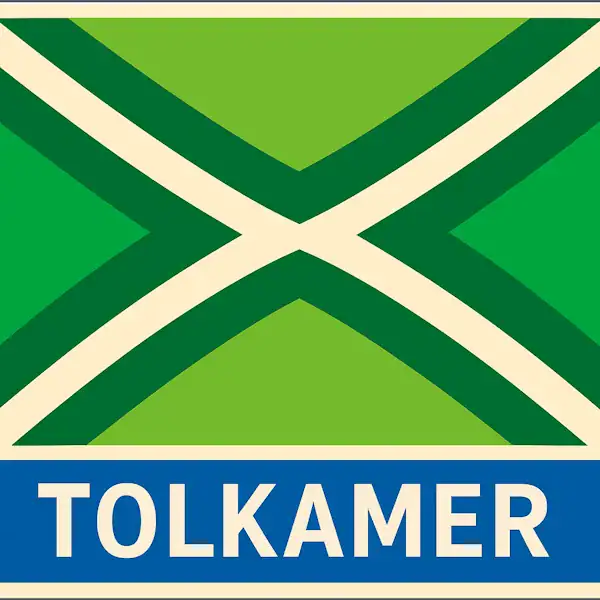Plaatsnaambord met de tekst "TOLKAMER" in witte hoofdletters op een blauwe balk. Daarboven een vlag met lichtgroene achtergrond, een helder wit St. Andrieskruis gecentreerd in een donkergroen kruispatroon — volgens het officiële ontwerp van de Achterhoekvlag.
